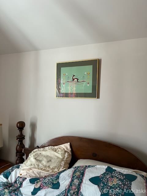 A framed artwork hangs above a cozy bed with pillows and a blanket.