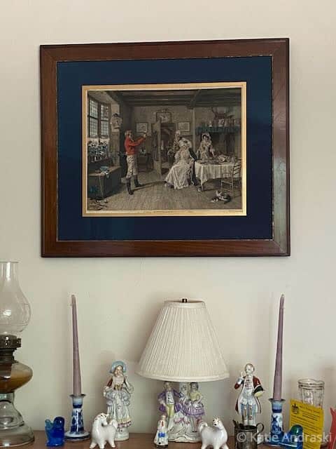 Vintage framed painting above a lamp on a white wall.