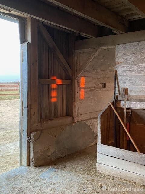 Warm orange light glows through barn window shutters at sunset.
