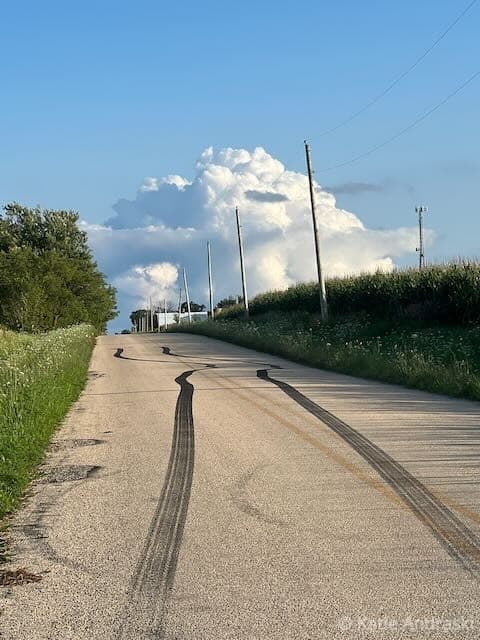 Rural road with tire tracks under a partly cloudy sky.