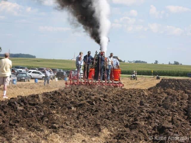 People gathered around a smoking tractor in a field event.