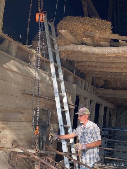 Man in plaid shirt working with wooden ladder in a rustic building.