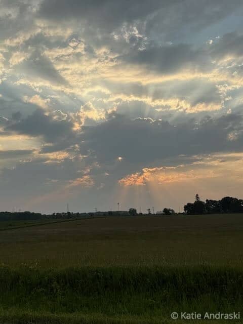 Sun rays break through dramatic clouds over a flat landscape at sunset.