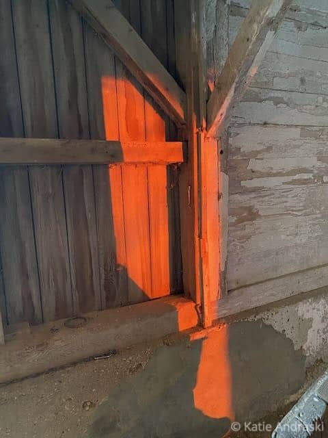 Orange light shining through barn door gaps onto wooden interior.