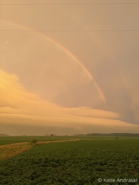 A rainbow arches over a serene landscape at sunset.