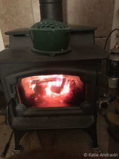 A cozy fire burns inside a black wood stove, casting a warm glow.