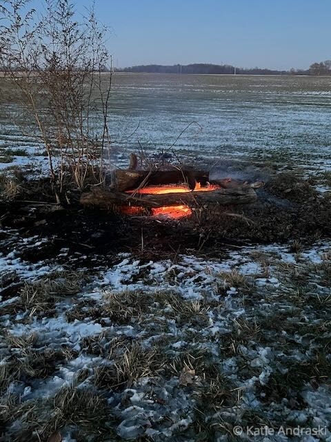A small fire burns in a snowy outdoor setting near a lake.